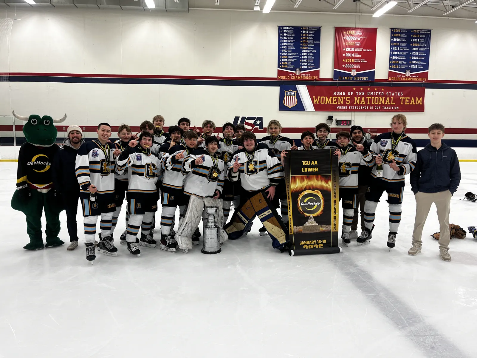 A boys team celebrating on the ice with the OneHockey Cup and their championship banner