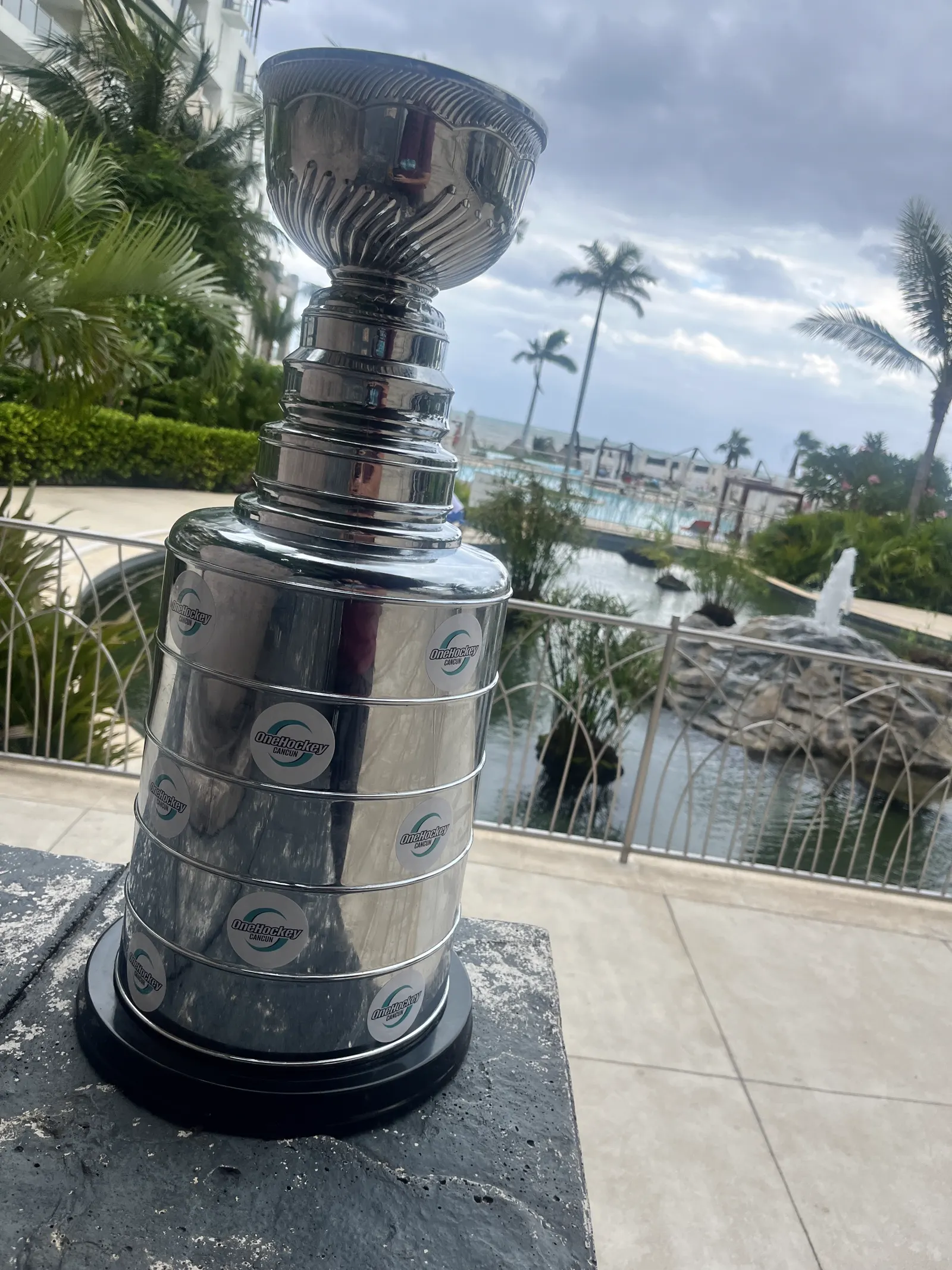 The OneHockey Cup standing outdoors in Cancún with palm trees and a lagoon behind it