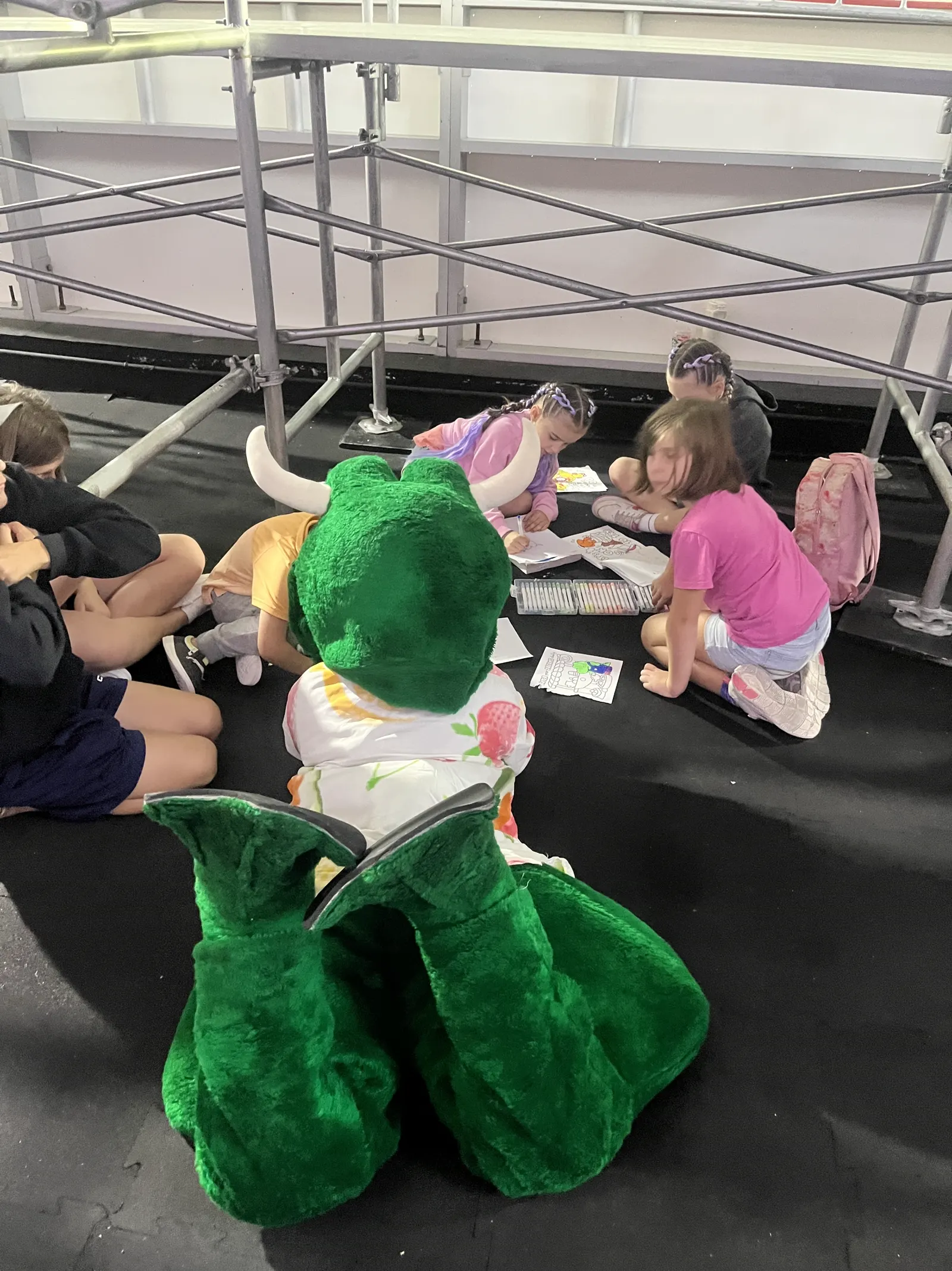 Freddie the mascot lying on the floor colouring with a group of children at the resort in Cancún