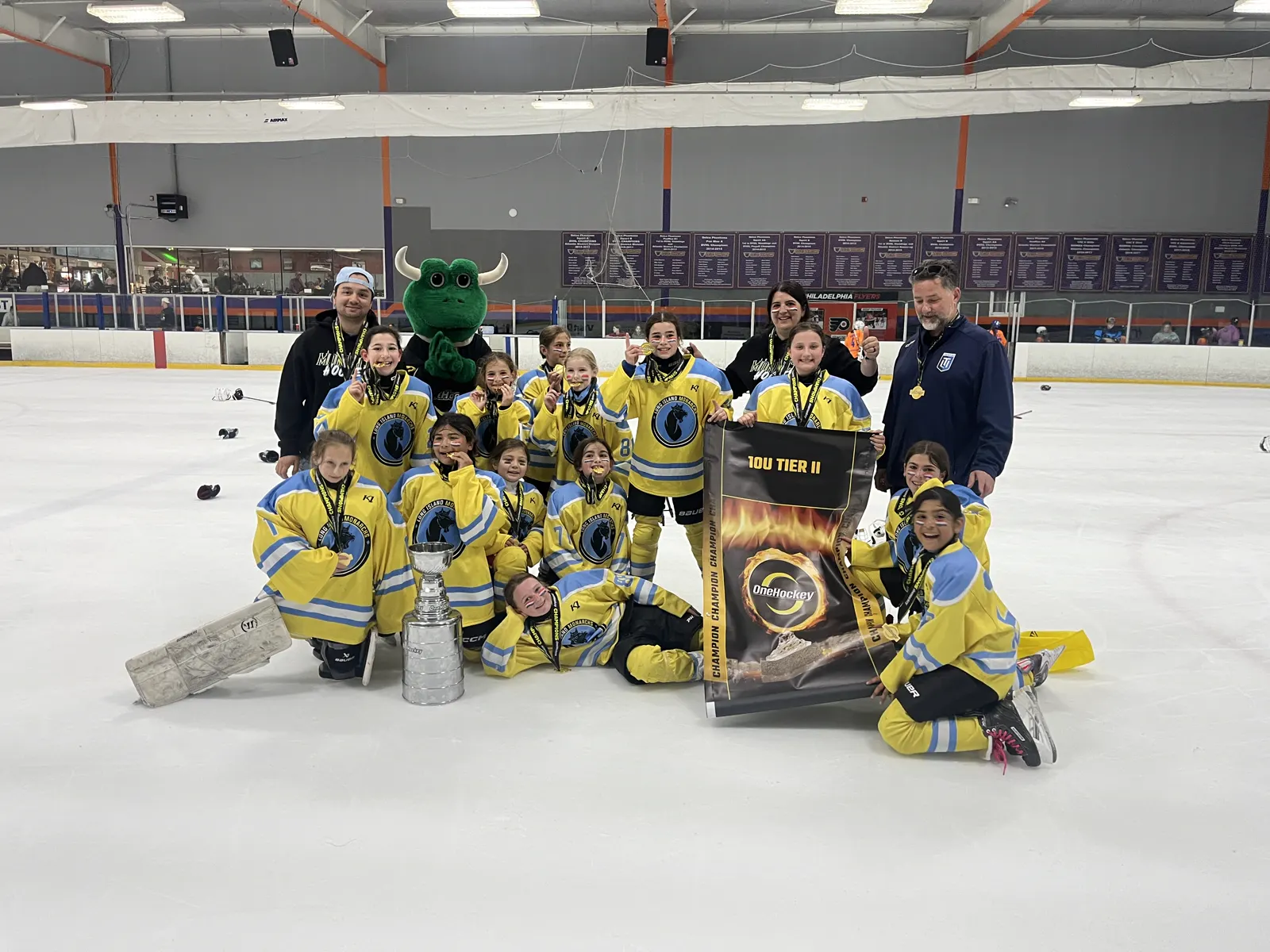 A girls team on the ice with Freddie, the OneHockey Cup and their Tier II championship banner