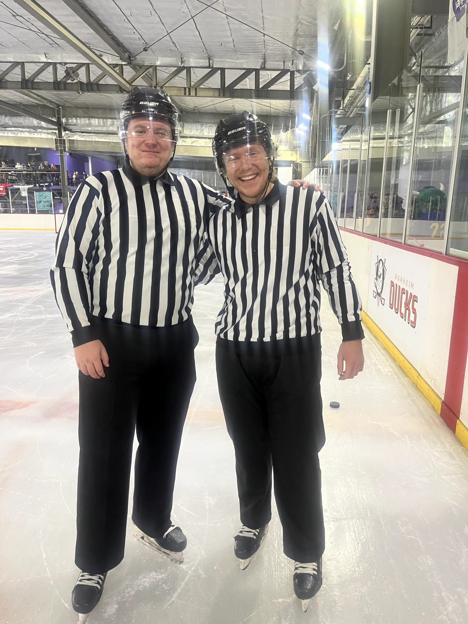 Two officials in striped jerseys standing on the ice at the Cancún rink